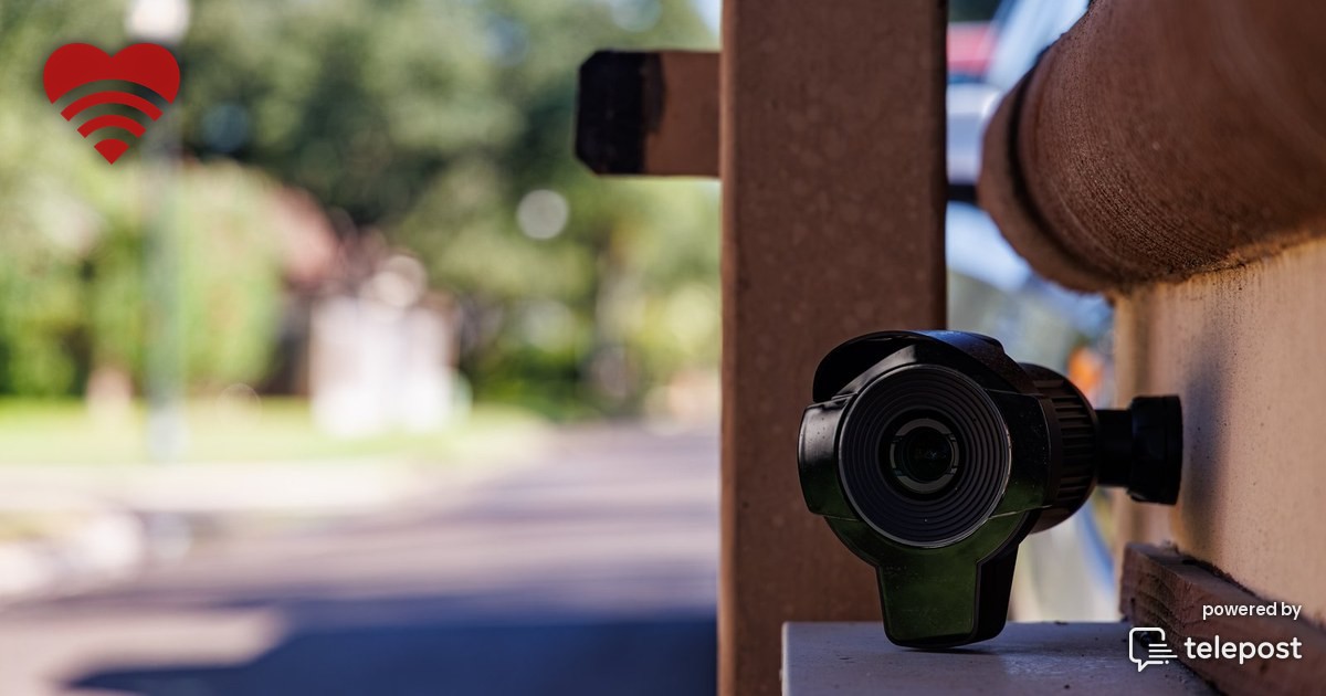 A license plate reader camera mounted on a pole at the entrance to a residential neighborhood, angled down toward the roadway at dusk.